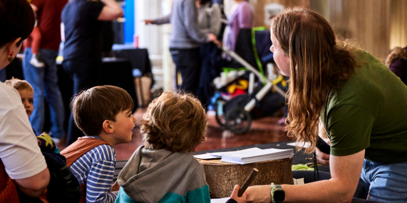 A woman speaks with two children at a stall at Be Curious Live.