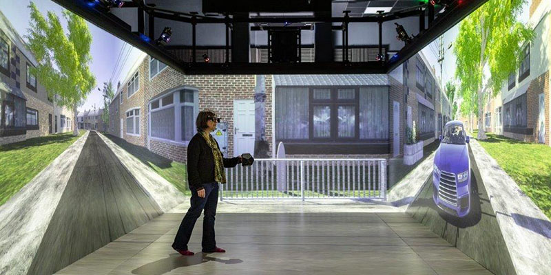 A person using the Driving Simulator environment. There is a projected scene of a road with the user interacting with surroundings.