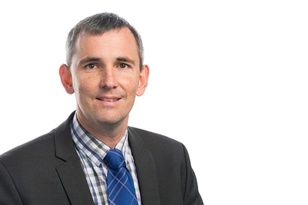 Headshot of Paul Baxter wearing a suit jacket, check shirt and blue tie.