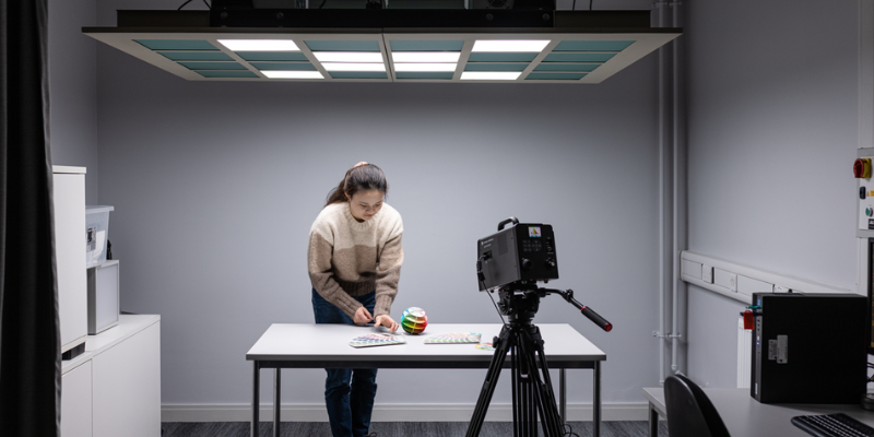 Technician demonstrating the lighting lab, under LED lights, using different colour charts in front of a camera.