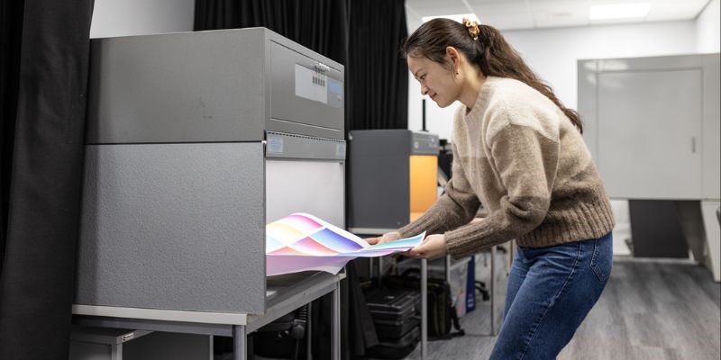 A technician pulling a colour chart our of a grey machine that assess colour.
