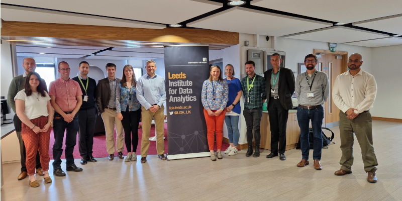 Group shot of staff from Asda and the University of Leeds around a pop-up poster for Leeds Institute for Data Analysis
