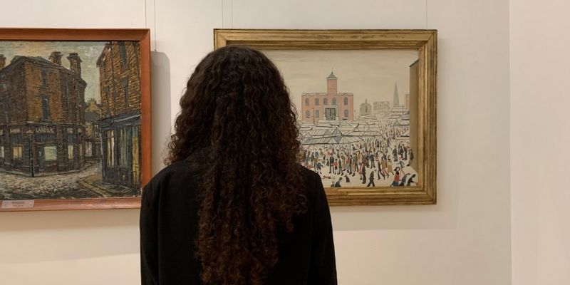 back of woman&#039;s head looking at lowry painting