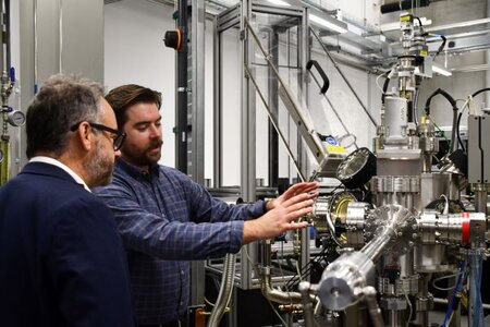 The Minister is looking into a camber device that is pumping the air out of materials to see how they react. Stood next to the Minister is a technician from The Royce Deposition Lab.