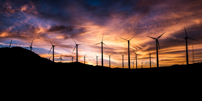 Wind turbines on a hill, silhouetted against a dramatic sky.