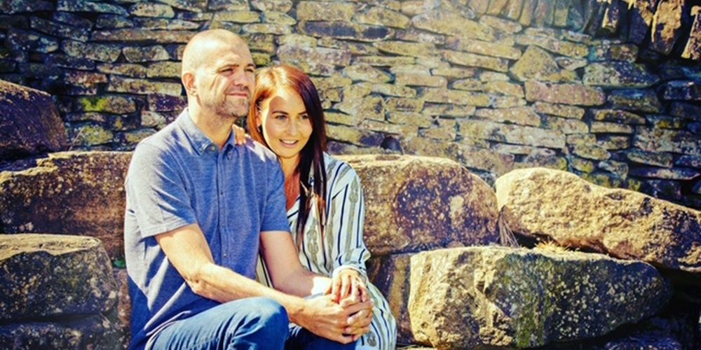 Man and women sit in front of stone wall holding hands