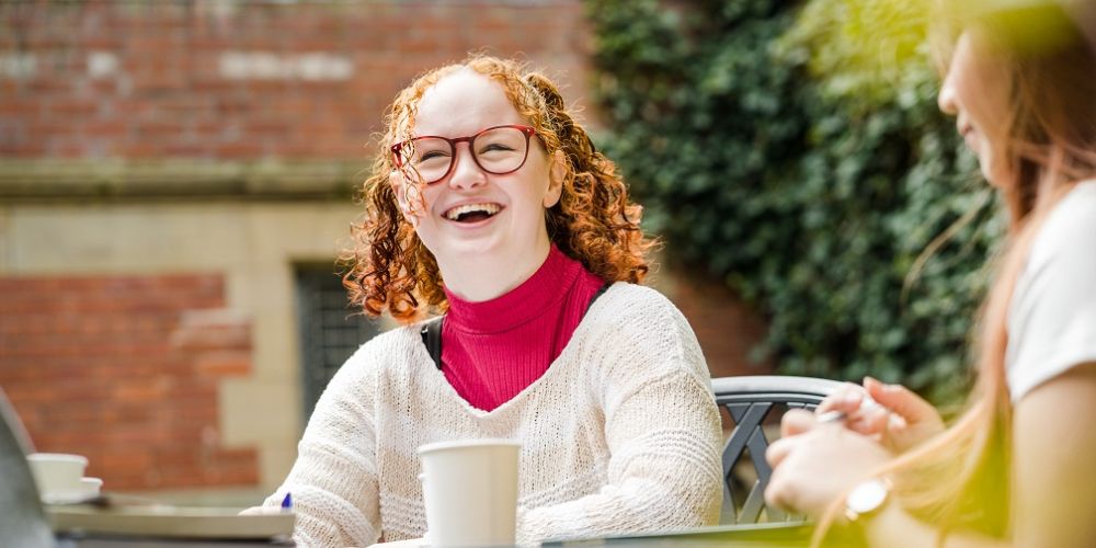 Two students sat in a courtyard cafe chatting and laughing