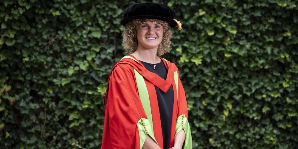 England Womens rugby player Ellie Kildunne wears red and green honorary graduate robes and smiles at the camera