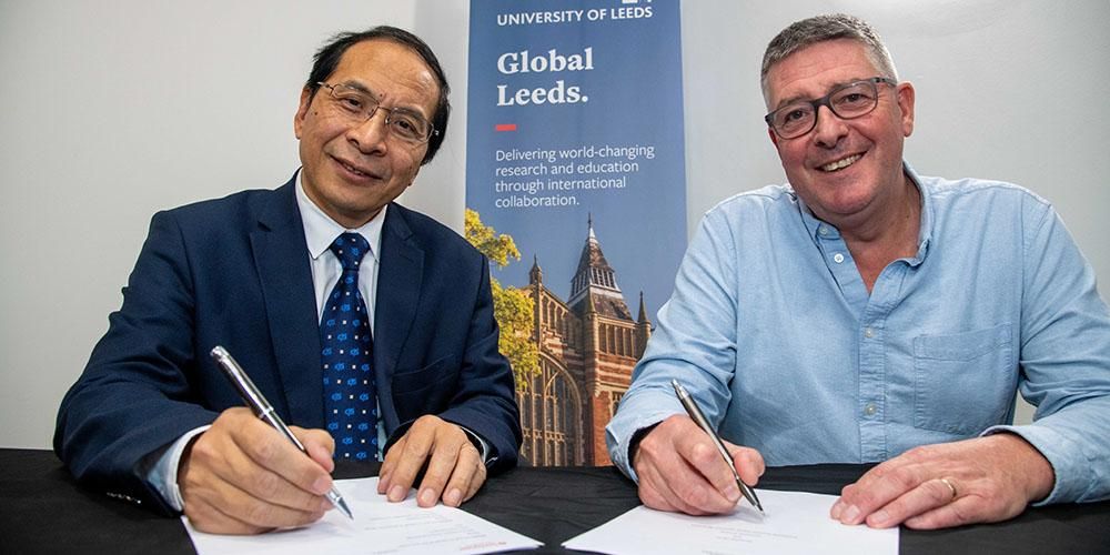 Professor Hai Sui Yu and Director of Santander Universities UK, Matt Hutnell signing paper agreements at a desk.