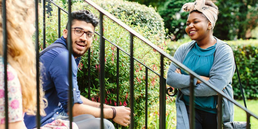 Three students in mid conversation on some steps with iron railings.