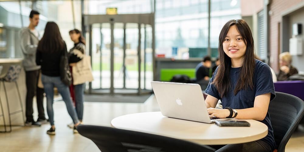 Student sat at a table with a laptop in Leeds University Business School.