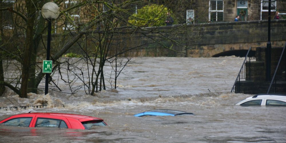 Three cars submerged in water as a street floods. Behind is a bridge, its arch nearly completely submerged in water.