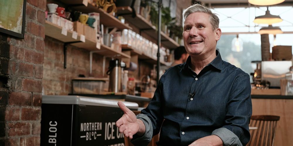 Keir Starmer sat in a cafe bar, smiling and gesturing with his hand.