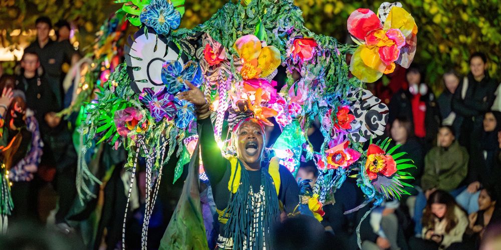 Copilot said:

Colourful flower-covered parade performer surrounded by a crowd at a night time festival.