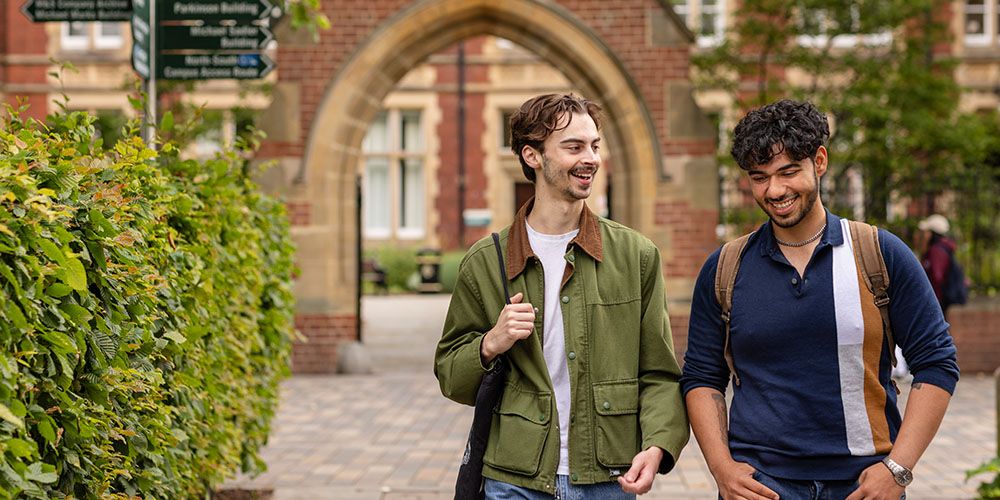 Two students walking beneath the brick archway of Clothworker's court, laughing and smiling.