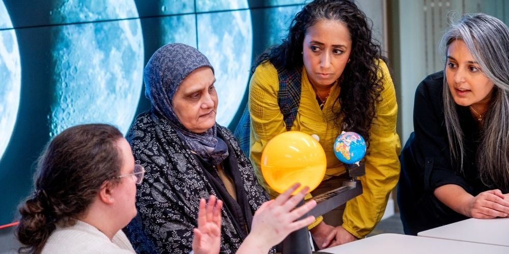 A group of people at the moonsighters course. They hold models of the sun and earth, and behind them are images of the moon.