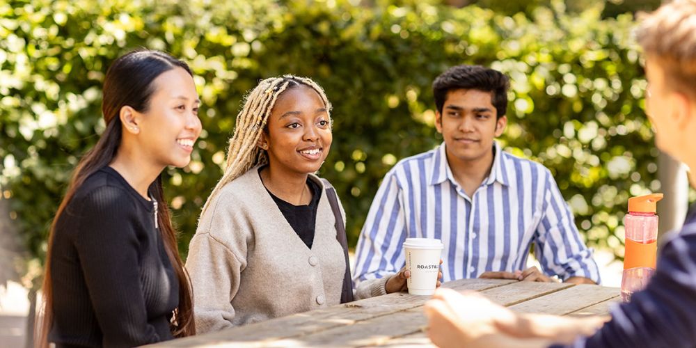 Three students sat outside drinking coffee.
