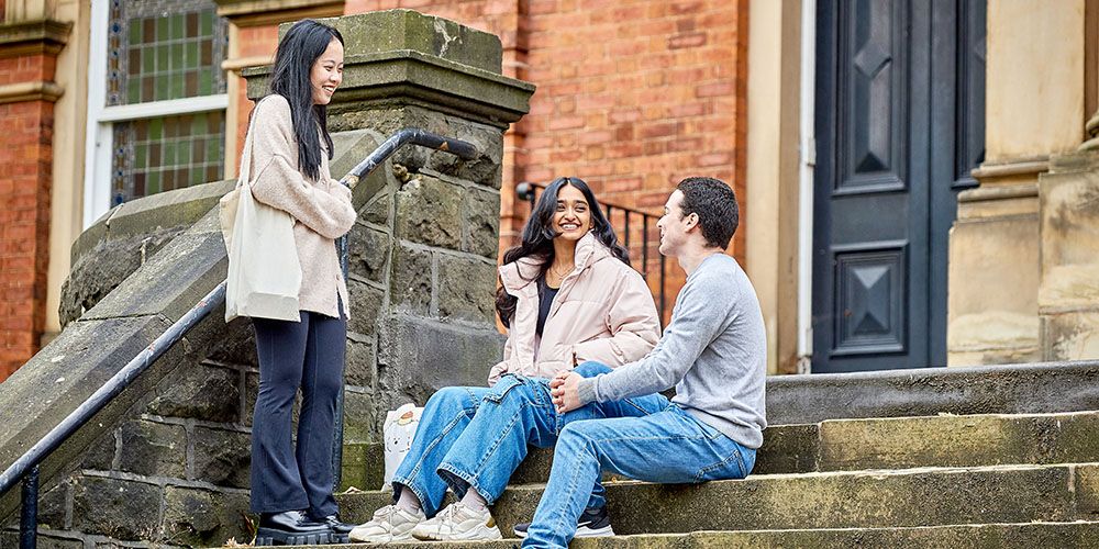 Three students smiling outside of a red brick terrace.