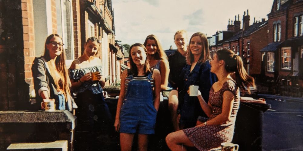 Anna sits upon a wall on a terraced street with friends laughing during the summer