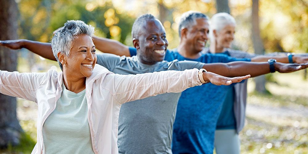 Four older people smiling while exercising outside in the sunshine.