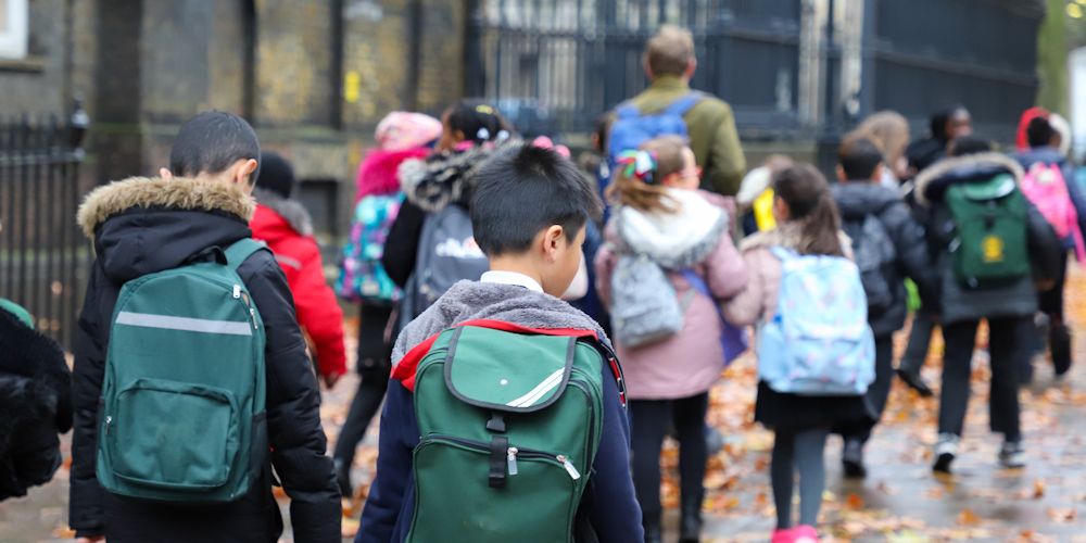 Group of school children walking down the street with a teacher on an autumn day.