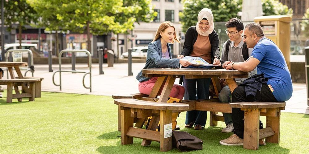 Students sitting on a picnic bench looking at a map outside Leeds Art Gallery