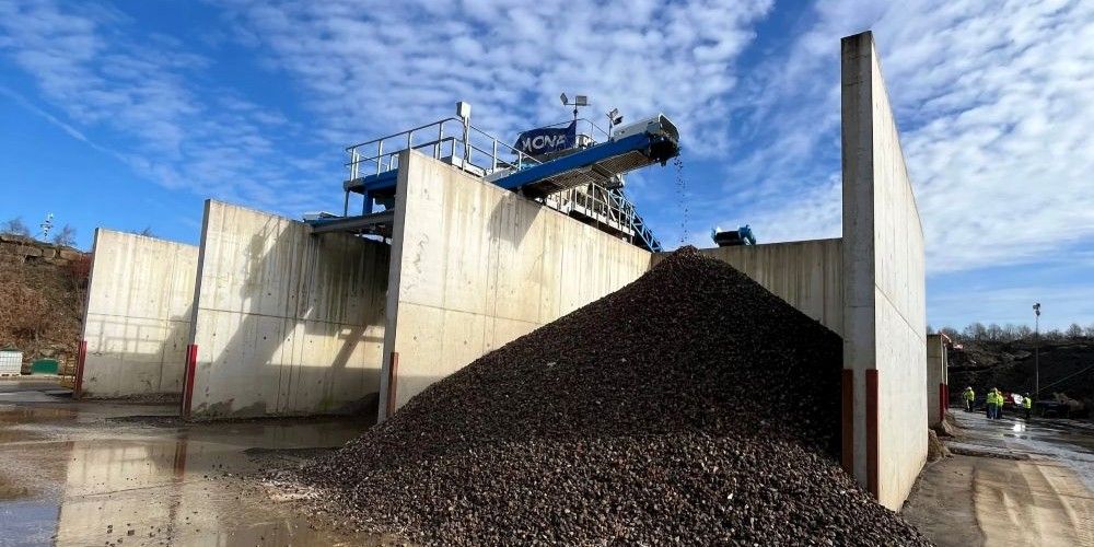 A large pile of clay cascades out of a concrete bay at a quarry.