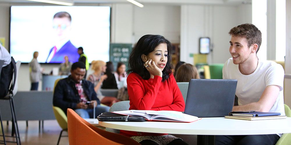 Students using a laptop and books in the open space of Leeds University Union.