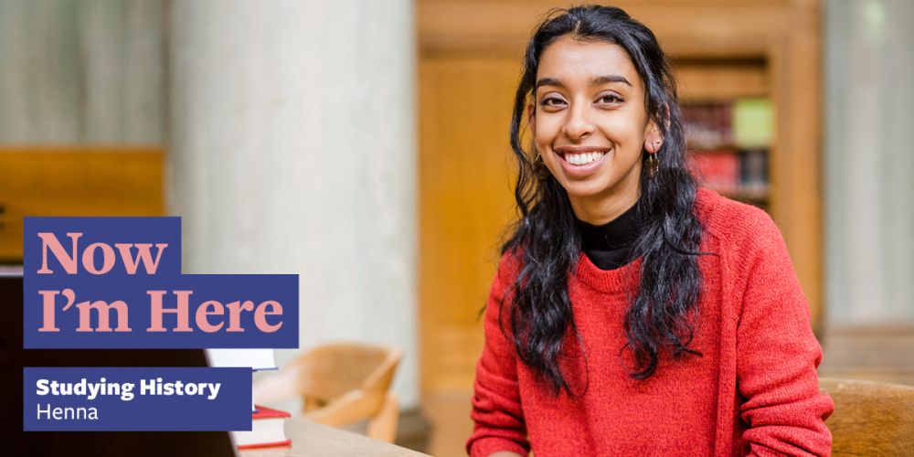 A student sat in a library with a shelf of books in the background. Text says: Now I'm Here studying History, Henna.