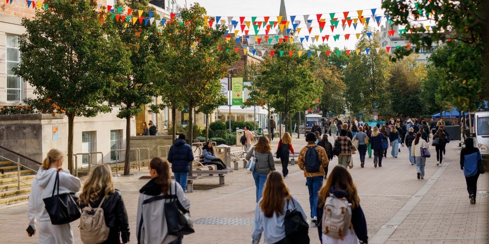 Students walk through the University of Leeds campus with bunting strung between buildings.