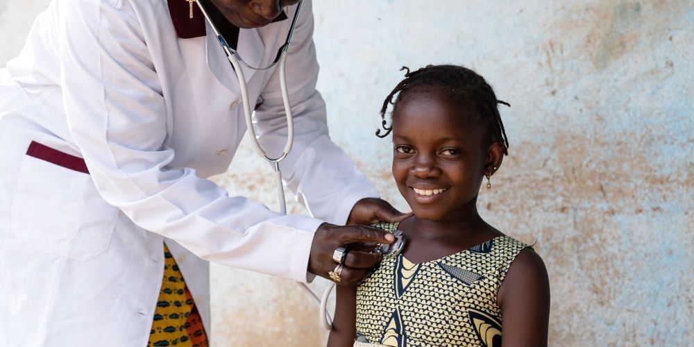 A health professional holding a stethoscope on a smiling child.