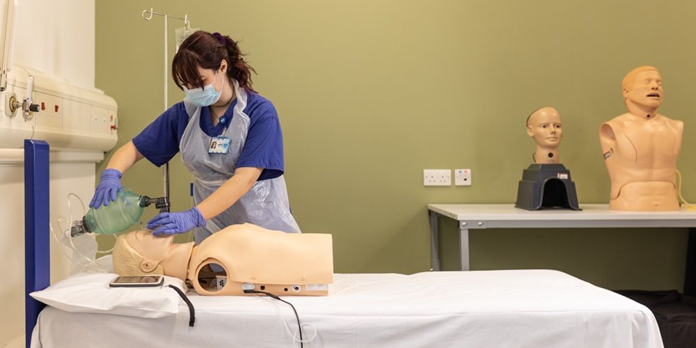 一名医科学生在医疗训练室练习将呼吸设备放在模拟患者身上。