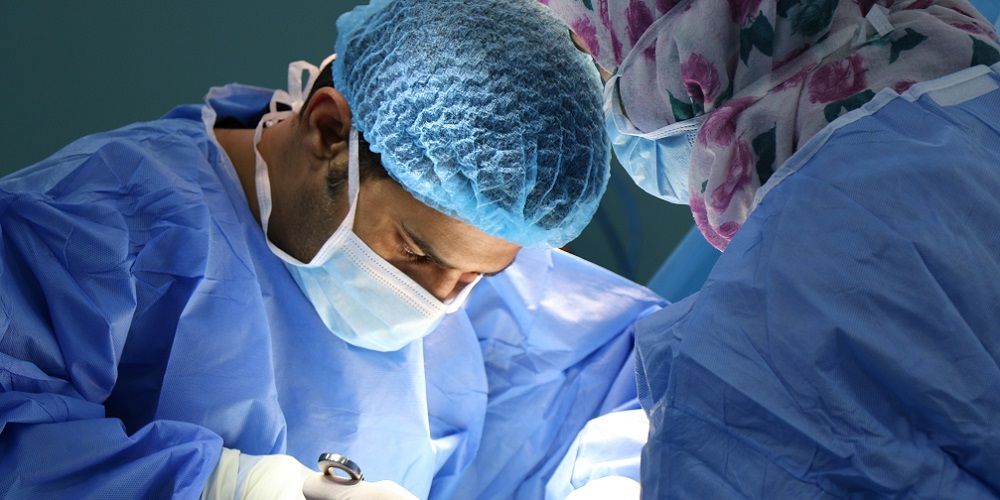 Two surgeons wearing blue protective gowns, face masks and hairnets carrying our a surgical procedure