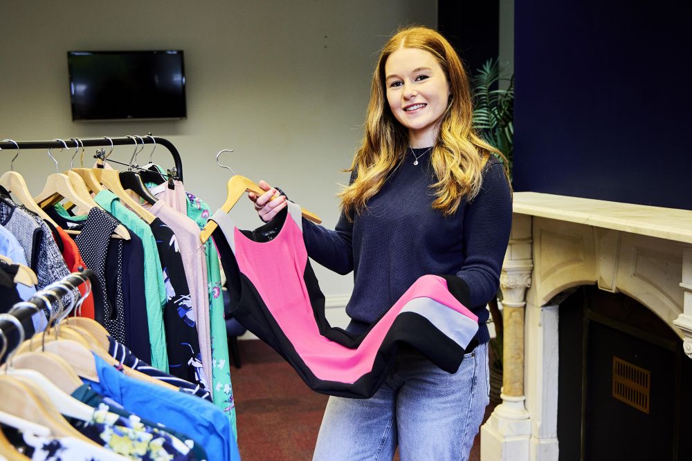 A person standing next to a clothes rack holding a dress on a hanger