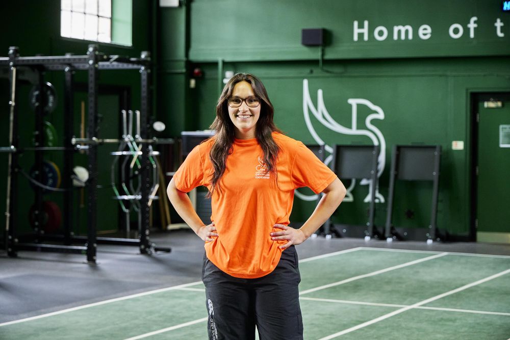 Person stood in a gym setting wearing a bright orange top