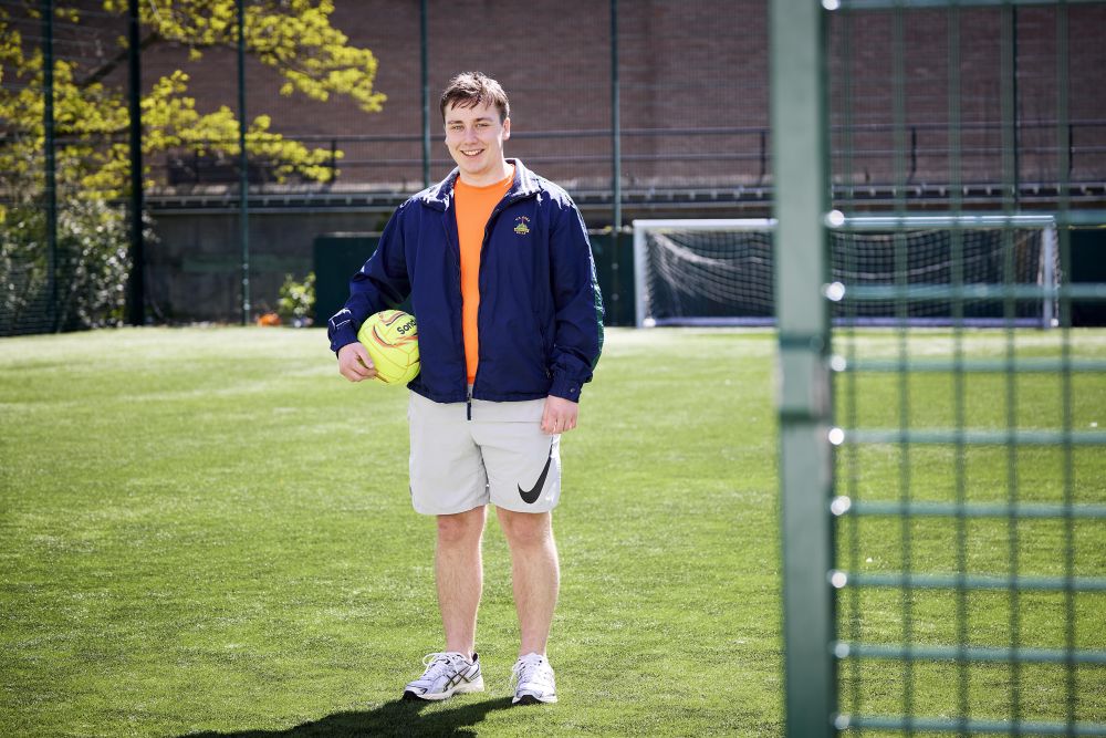 A person standing on a football pitch holding a football