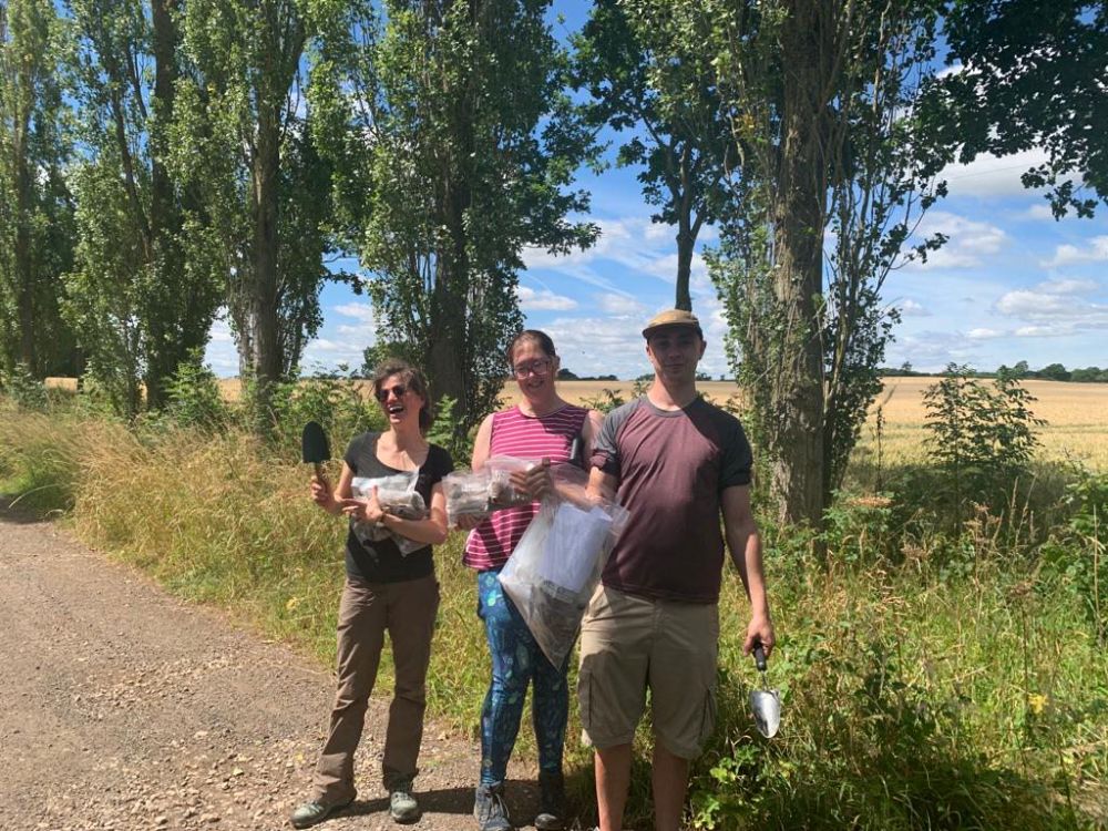 Three people pictured in the countryside holding trowels and bags of soil samples