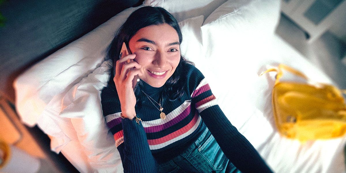 Student sat on a bed smiling on her mobile phone.