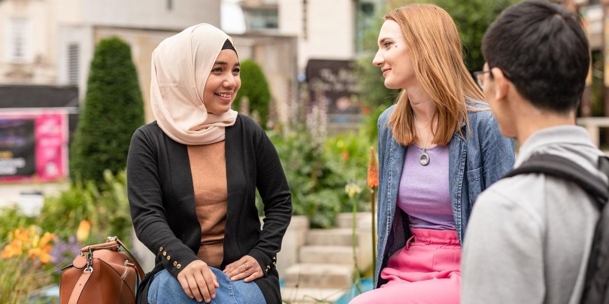 Three students in conversation in Leeds City Centre. 2 are sat on a wall.