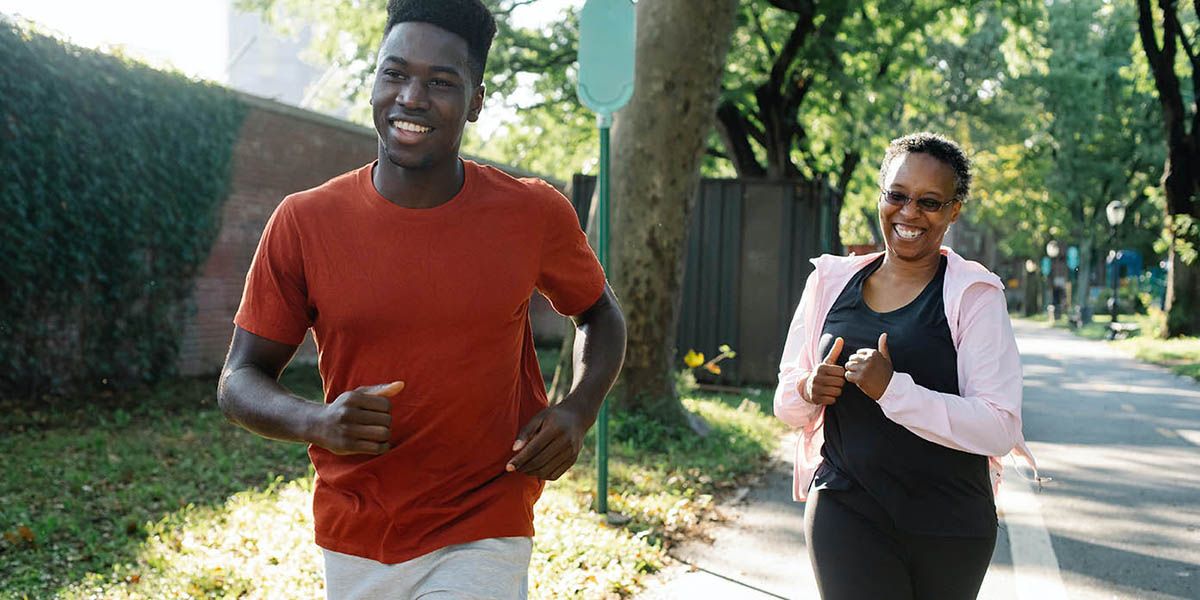 Two people jogging down a leafy, sunny, suburban pavement.