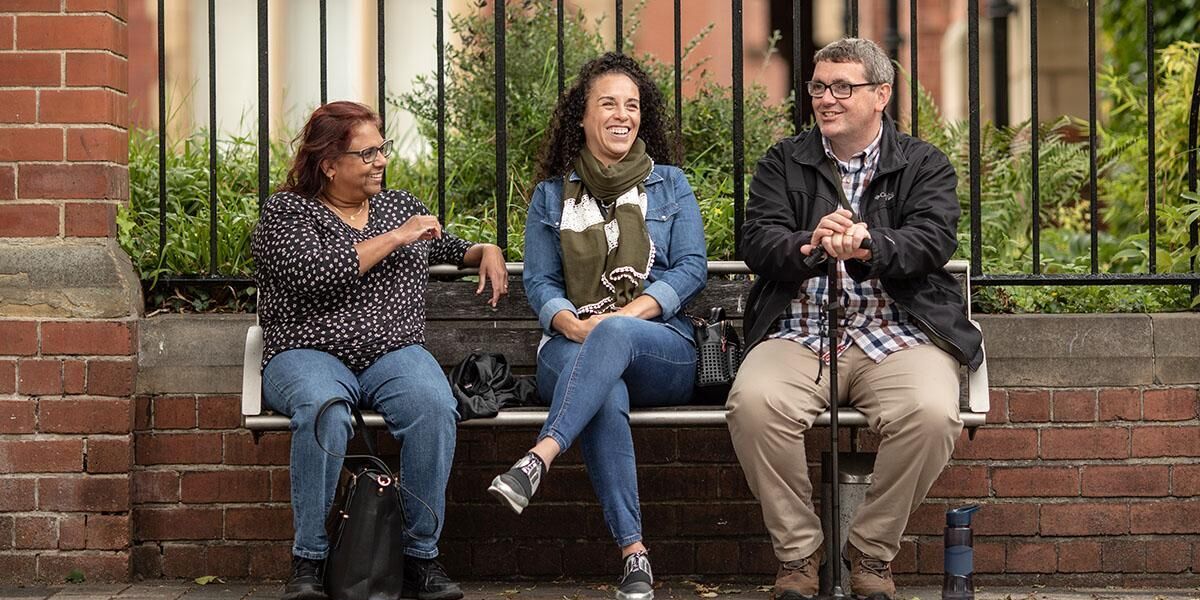 Three people sitting on a bench outside Clothworkers' Court