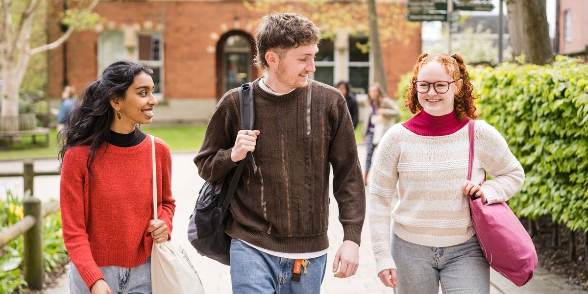 Three students walking on campus, chatting and smiling.