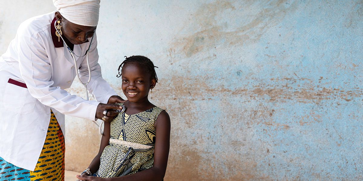 A smiling young girl being treated by a physician using a stethoscope.