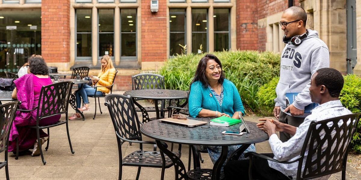 Three postgraduate researchers chat in courtyard cafe on campus
