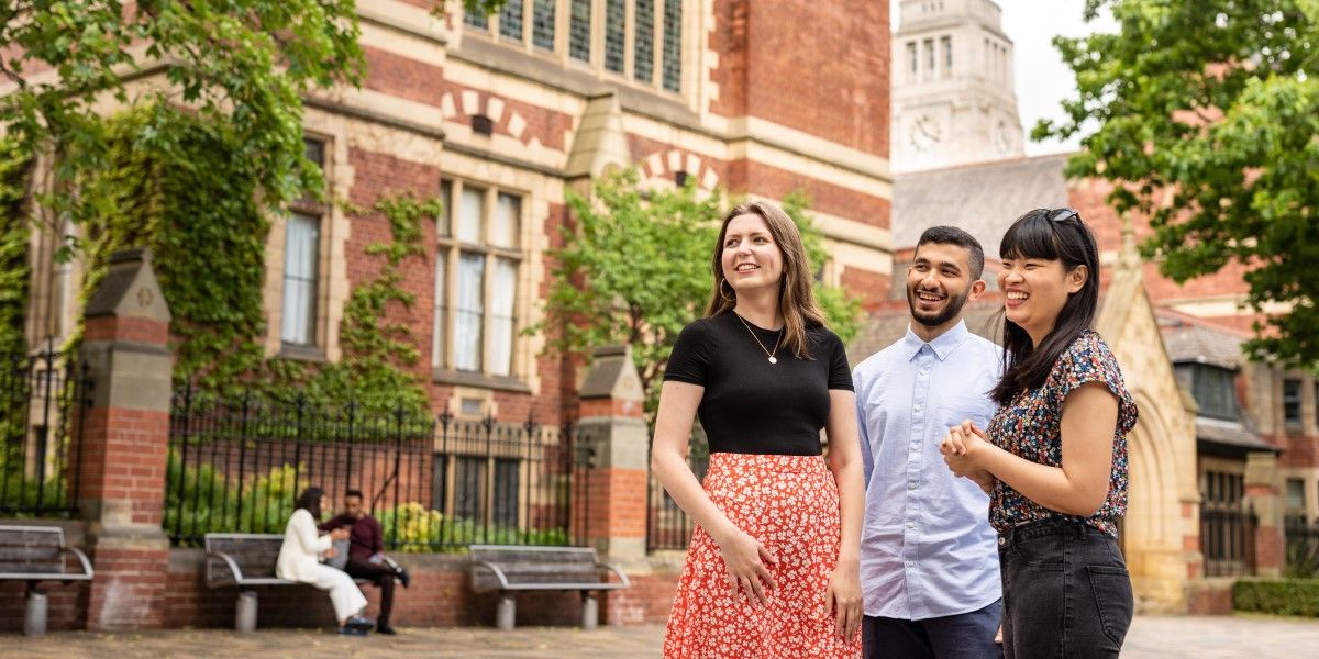 Three smiling students outside the red-brick Clothworkers' Building, with the white stone Parkinson tower in the background.