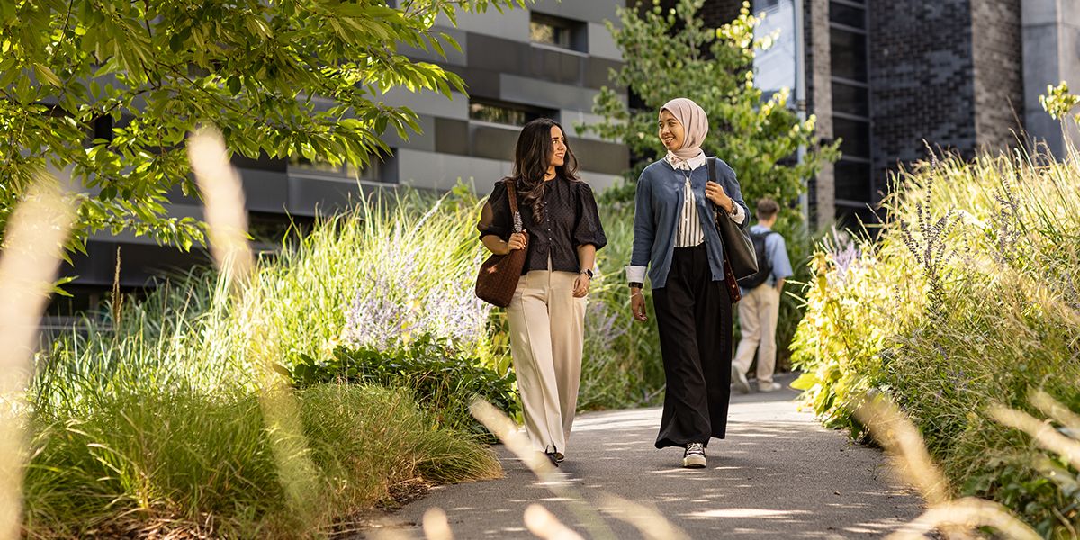 Two postgraduate students walking through a leafy path in front of the Stage at Leeds building.