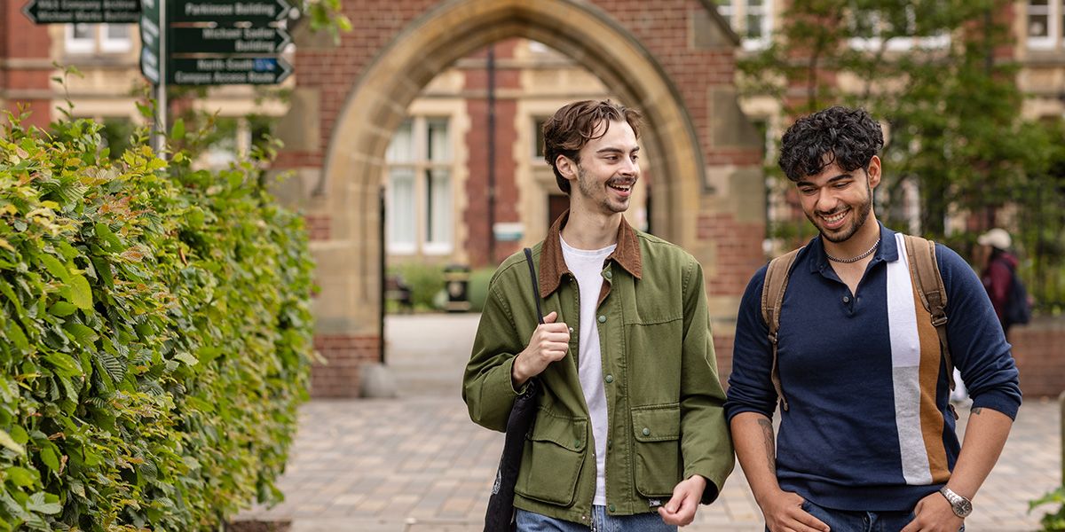 Two students walking through the red brick arch of Clothworker's Court on campus.