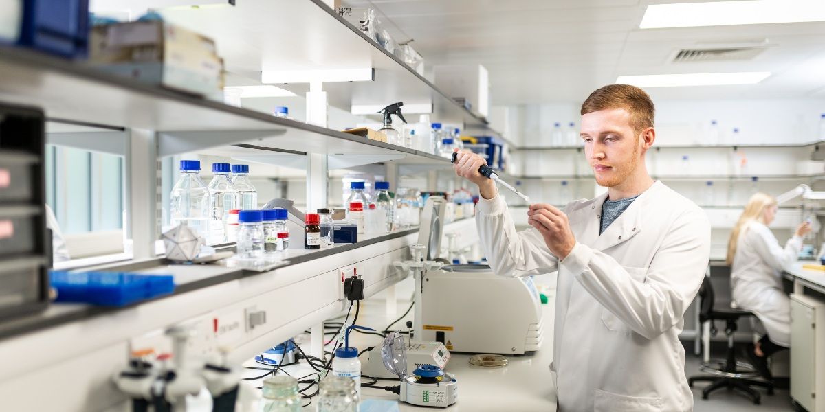 A researcher using lab equipment, wearing a protective lab coat.