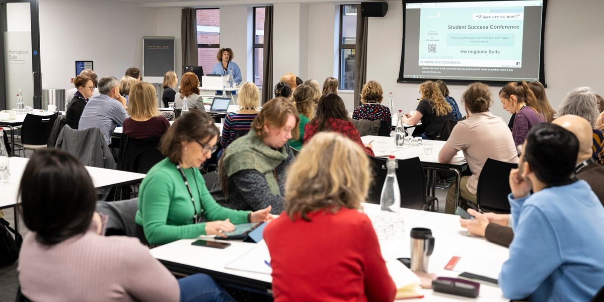 Delegates sat around tables at a University of Leeds Student Success conference listening to a presenter.