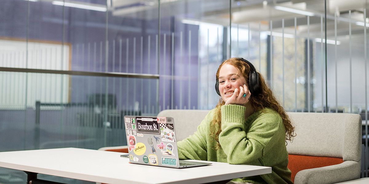 A student sat at a table using a laptop with a headset.